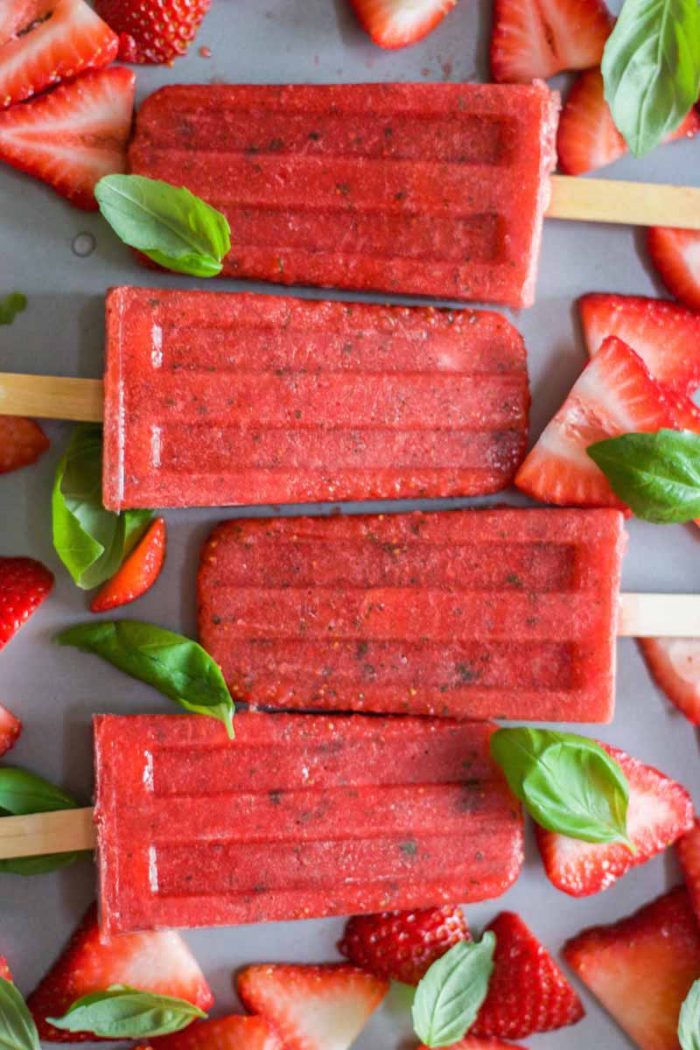 Strawberry Basil Popsicles alternating directions with strawberry slices and basil leaves on a sheet pan