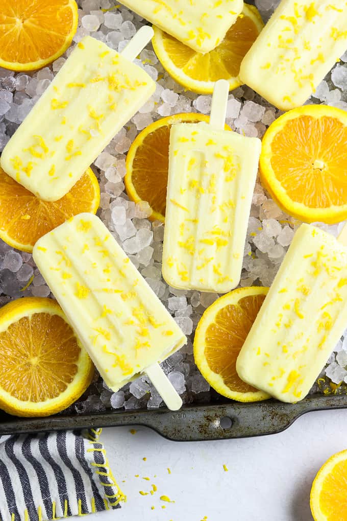 Orange creamsicle popicles and orange slices laying on a sheetpan of ice