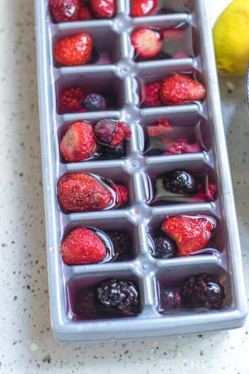 Ice cube tray filled with water and berries.