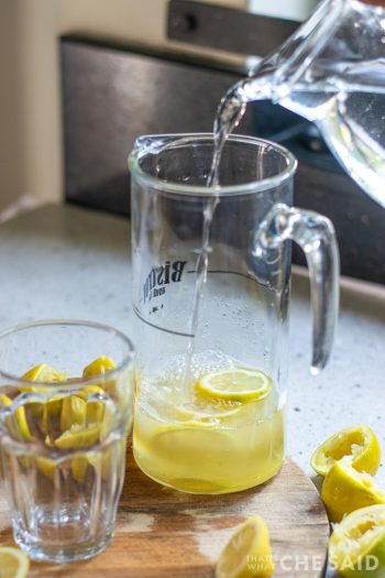 Pouring water in a pitcher filled with lemons and lemon juice.