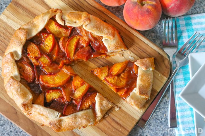 Peach Galette with slice removed on bamboo cutting board with forks and plates