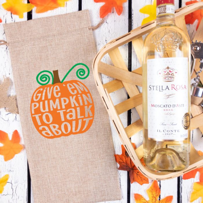 Burlap Wine Bottle Bag with Free Pumpkin SVG with iron on next to basket with some wine.  Fall leaves in background. 
