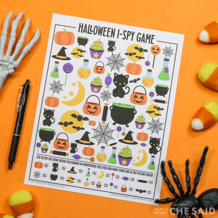 Orange background with Halloween I-spy printable and a pen and halloween decorations around it - square orientation