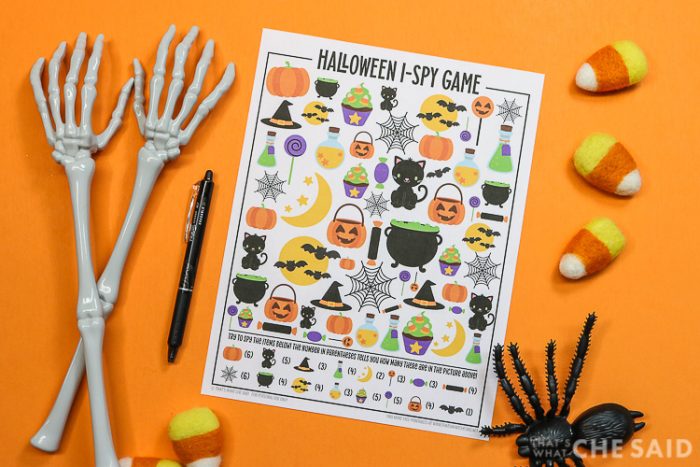 Orange background with Halloween I-spy printable and a pen and halloween decorations around it - horizontal orientation