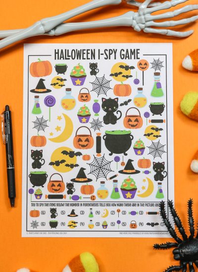 Orange background with Halloween I-spy printable and a pen and halloween decorations around it - vertical orientation