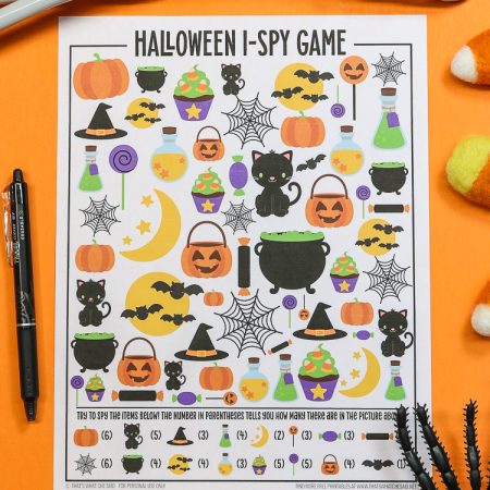 Orange background with Halloween I-spy printable and a pen and halloween decorations around it - vertical orientation