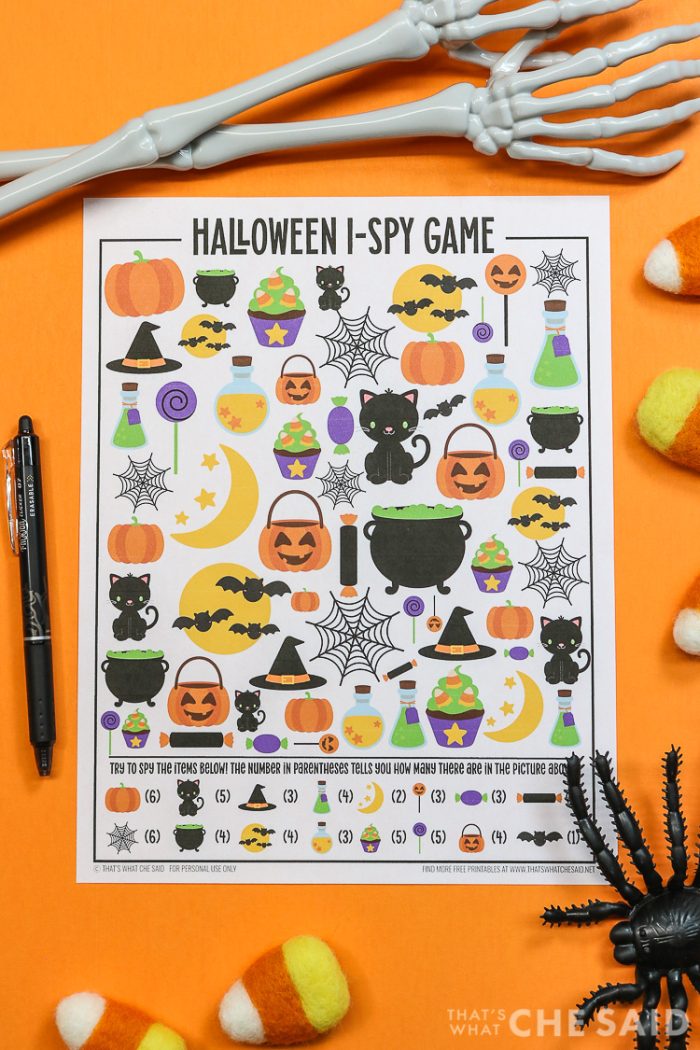 Orange background with Halloween I-spy printable and a pen and halloween decorations around it - vertical orientation