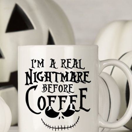 White mug with black and white halloween decor behind. Mug Reads" I'm a Real Nightmare Before Coffee"