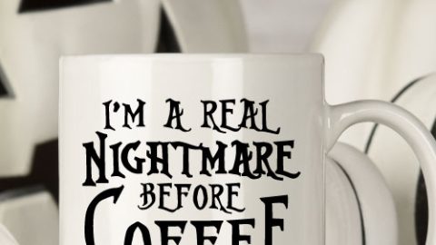 White mug with black and white halloween decor behind. Mug Reads" I'm a Real Nightmare Before Coffee"