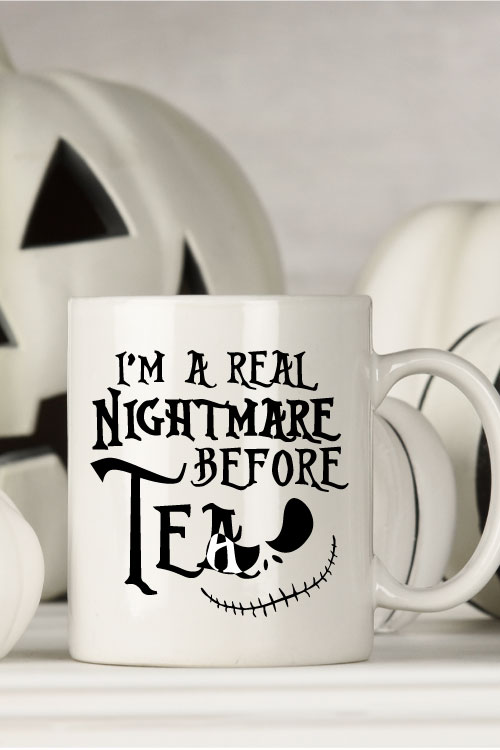White mug with black and white halloween decor behind. Mug Reads" I'm a Real Nightmare Before Tea"