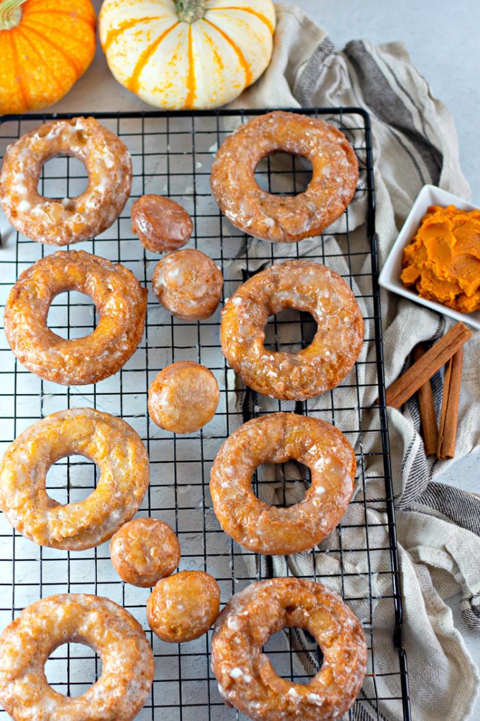 Pumpkin donuts and pumpkin donut holes on a black wire cooling rack with pumpkins, pumpkin puree and cinnamon sticks