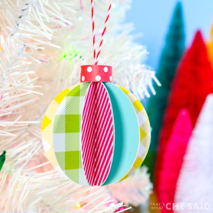 Blue Background, white artificual tree with bottle brush trees in background. Foreground is 3D paper ornament - square orientation