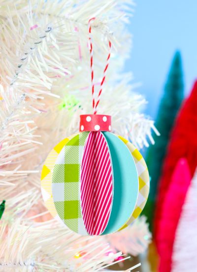 Blue Background, white artificual tree with bottle brush trees in background. Foreground is 3D paper ornament - vertical orientation