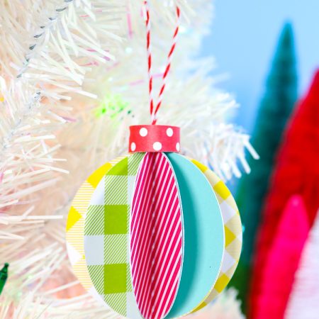 Blue Background, white artificual tree with bottle brush trees in background. Foreground is 3D paper ornament - vertical orientation