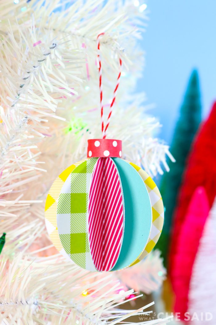 Blue Background, white artificual tree with bottle brush trees in background. Foreground is 3D paper ornament - vertical orientation