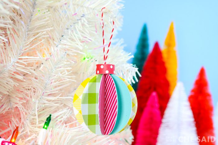 Blue Background, white artificual tree with bottle brush trees in background. Foreground is 3D paper ornament - horizontal orientation