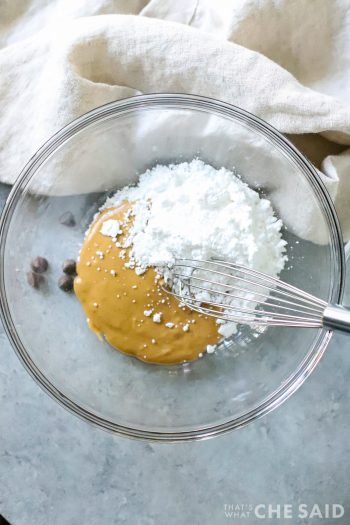 Glass bowl with peanut butter and powdered sugar and whisk
