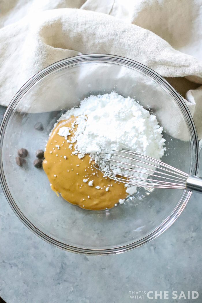 Glass bowl with peanut butter and powdered sugar and whisk
