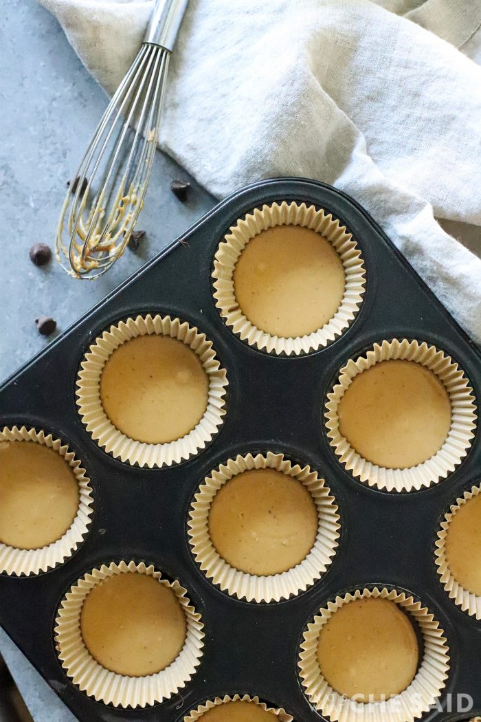 Cupcake tin with liners that has peanut butter mixture layered on top of chocolate layer