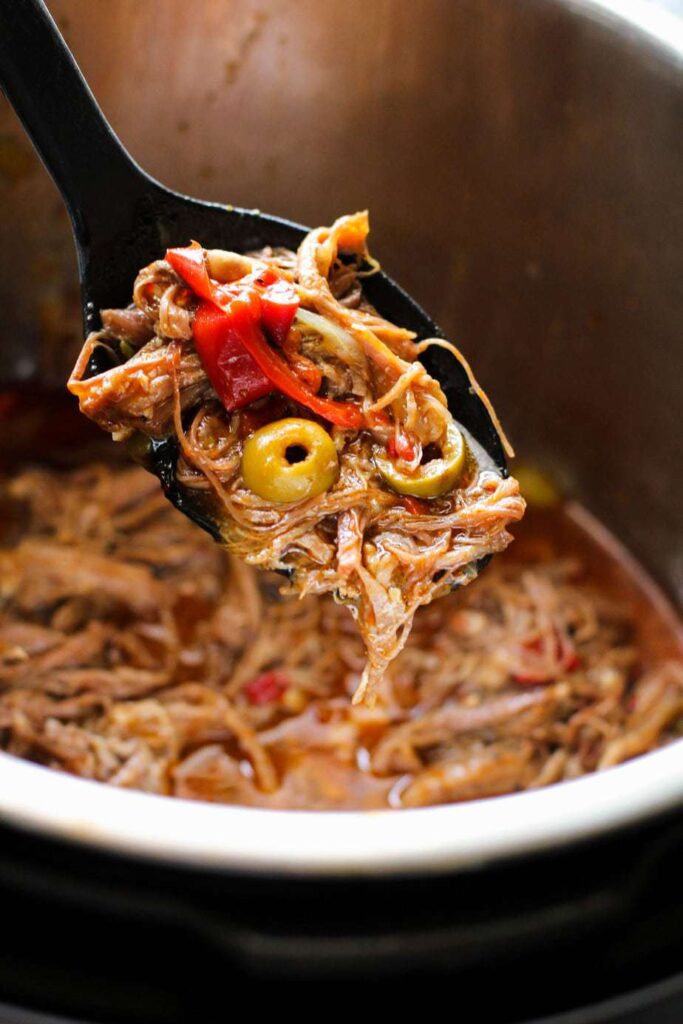 Serving spoon full of Cuban Ropa Vieja over the inner pot of the instant pot