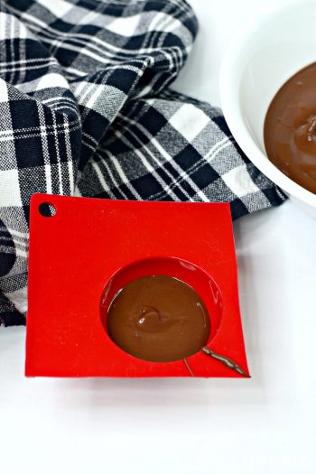 Bowl of melted chocolate and half sphere silicone mold and spoon. Mild is filled with chocolate