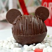 Chocolate Hot Chocolate Bomb with added chocolate wafers as ears to resemble Mickey Mouse with marshmallows and Christmas decor in background horizontal orientation