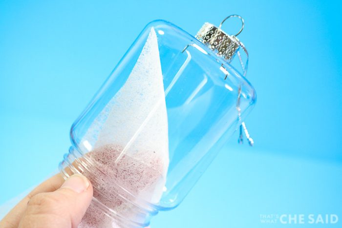 Showing how to wipe the inside of a plastic ornament with a dryer sheet to reduce static for fake snow.
