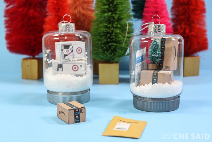 Two snow globe jar ornaments. One has miniature target boxes and one has miniature Amazon boxes and envelopes