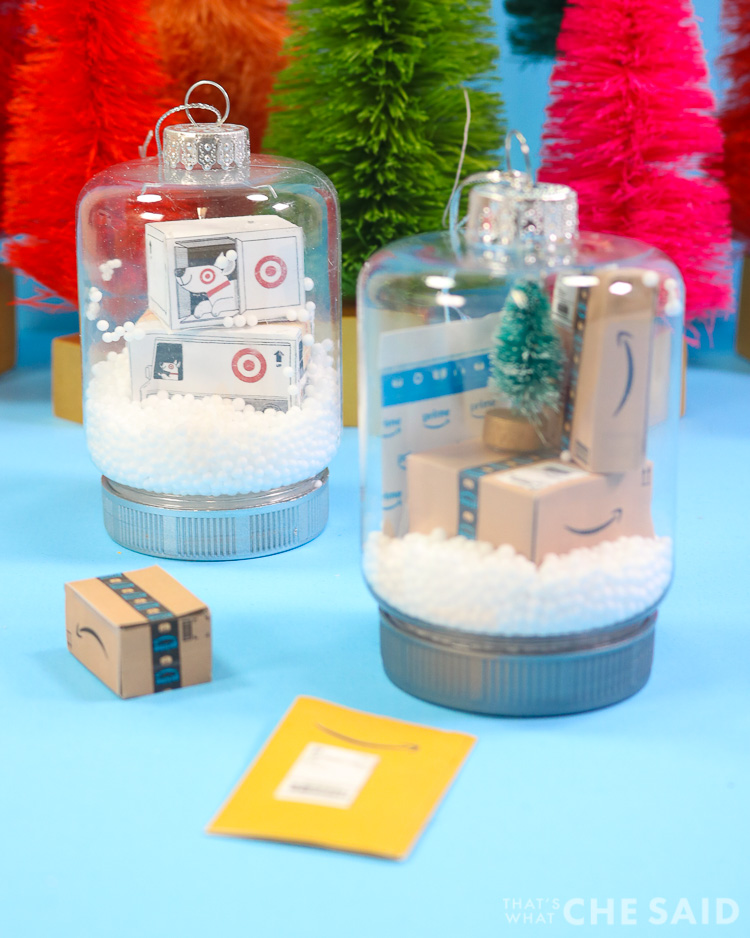 Two snow globe jar ornaments. One has miniature target boxes and one has miniature Amazon boxes and envelopes Vertical Orientation