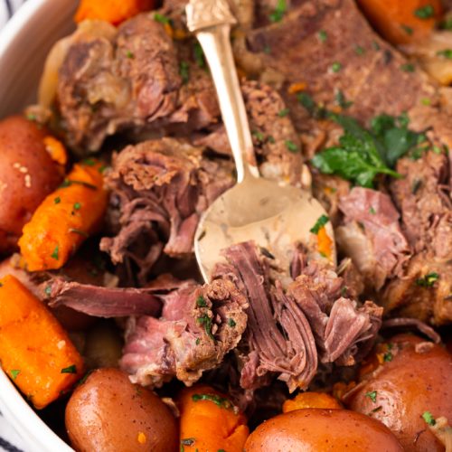 Fork lifting tender pot roast made in the instant pot with full roast and potatoes and carrots