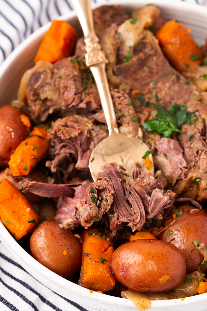 Fork lifting tender pot roast made in the instant pot with full roast and potatoes and carrots