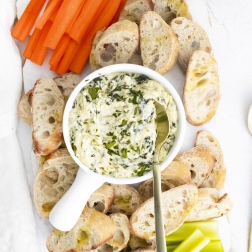 Spinach Dip in a bowl with crostini, carrots and celery around it.