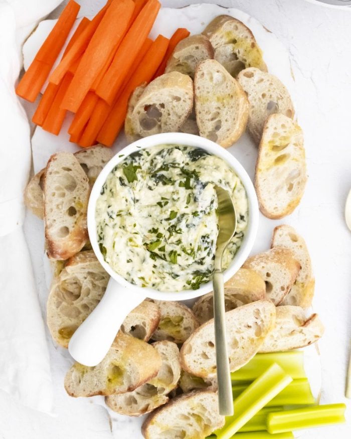 Spinach Dip in a bowl with crostini, carrots and celery around it.