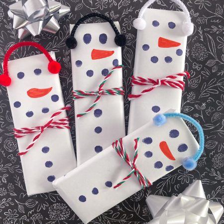 4 snowman candy bars on black background with bows vertical format