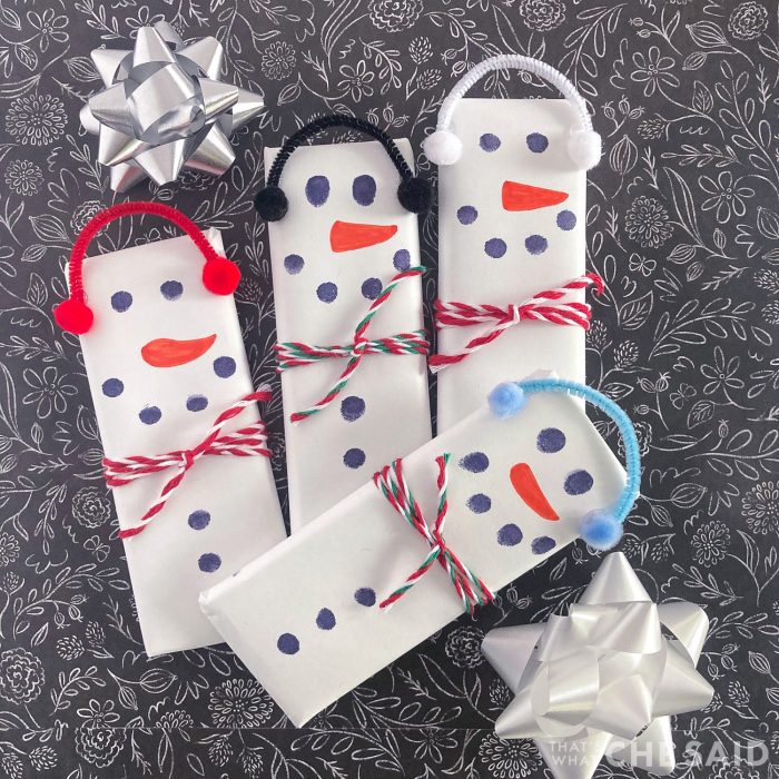 4 snowman candy bars on black background with bows square format