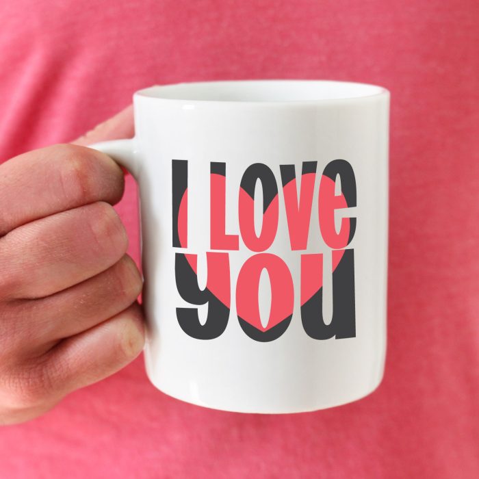 woman with pink shirt holding white coffee mug with a "I love you" blockout design