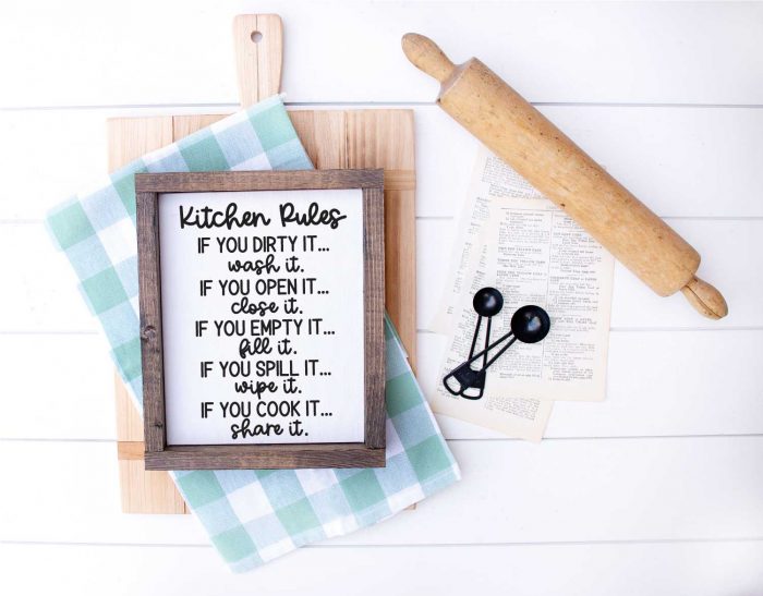 White wood with Cutting Board, kitchen towel, meansuring spoons, rolling pin and sign that has kitchen rules svg applied in horizontal format