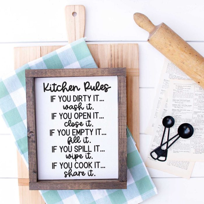 White wood with Cutting Board, kitchen towel, meansuring spoons, rolling pin and sign that has kitchen rules svg applied in Square format