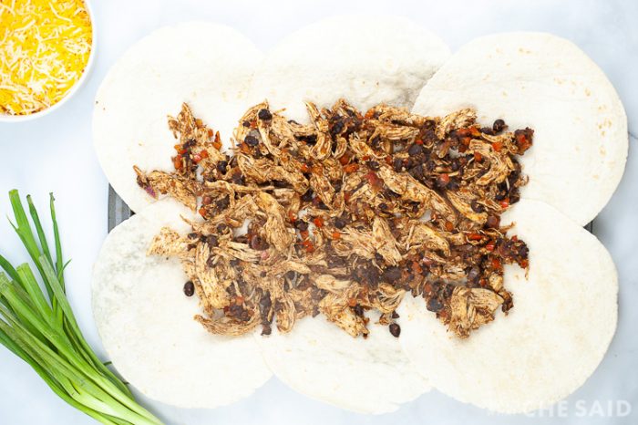 Toppings added to tortillas that are laid out on a sheet pan