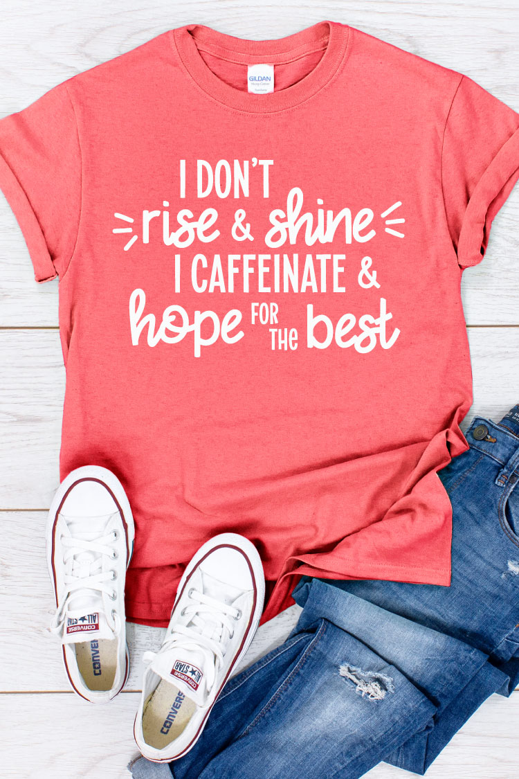 Coral shirt, jeans and white converse with "I don't rise and shine I caffeinate and hope for the best" written on the shirt in vertical format