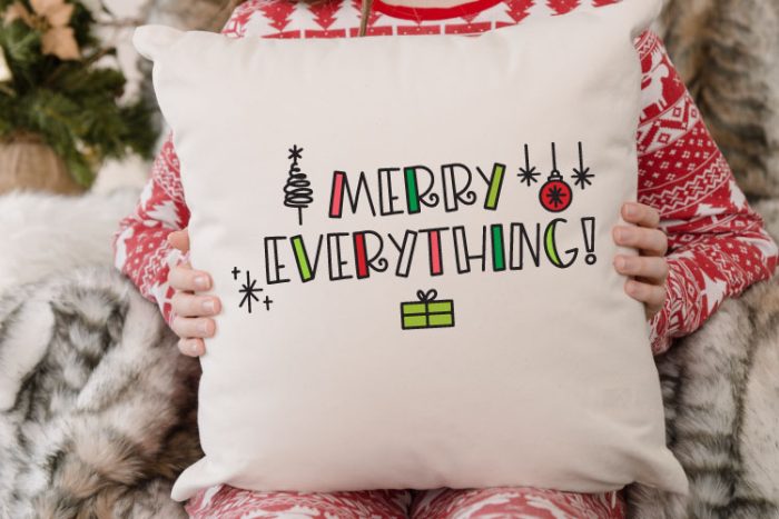 Child in CHristmas Jammies holding white pillow that reads Merry Everything