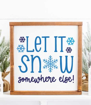 Let it Snow Somewhere else painted blue on a white background sign with a wooden frame