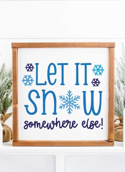 Let it Snow Somewhere else painted blue on a white background sign with a wooden frame