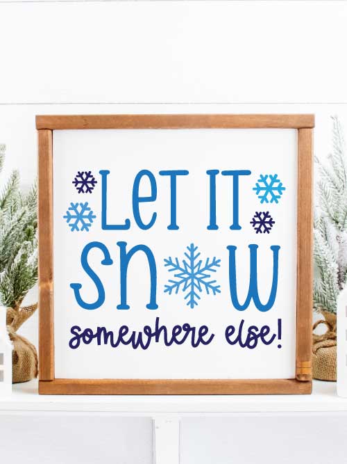 Let it Snow Somewhere else painted blue on a white background sign with a wooden frame