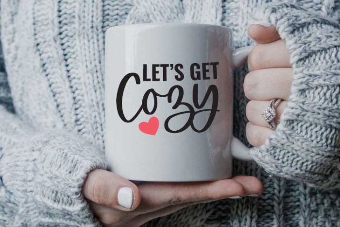 White Coffee Mug held by woman in sweater with "Let's Get Cozy" in vinyl