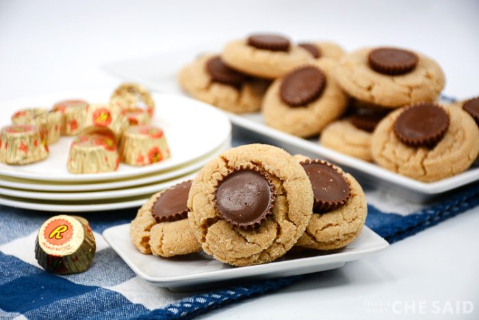 Peanut butter cookies with peanut butter cups candy pressed to the center with Reese's Peanut butter cups in background