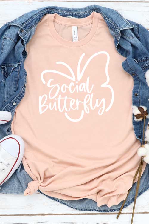 Peach T-shirt with Social Butterfly Design with Demin shirt behind and White Converse - Vertical Format