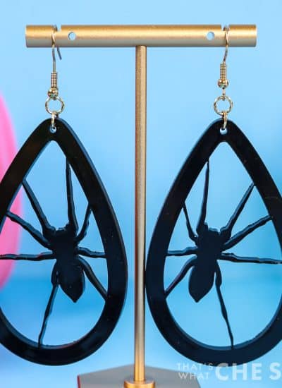 Black acrylic spider earrings hanging from a gold earring stand