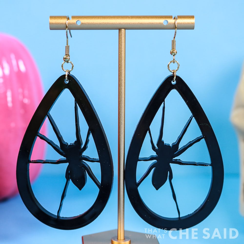 Black acrylic spider earrings hanging from a gold earring stand