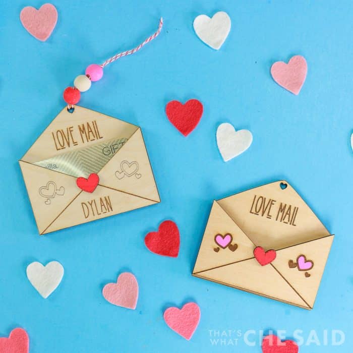 Blue background with heart confetti and two laser engraved and cut wooden gift card holders with valentine's day theme - square orientation